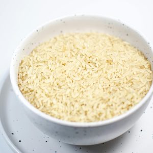 A close-up shot of uncooked rice grains in a speckled white bowl on a matching plate.