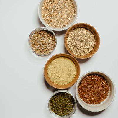 Top view of various seeds and grains displayed in ceramic bowls on a white background.